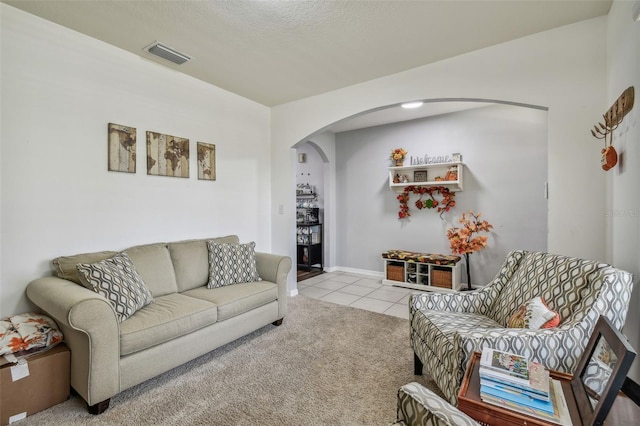 living room featuring arched walkways, carpet flooring, visible vents, and tile patterned flooring