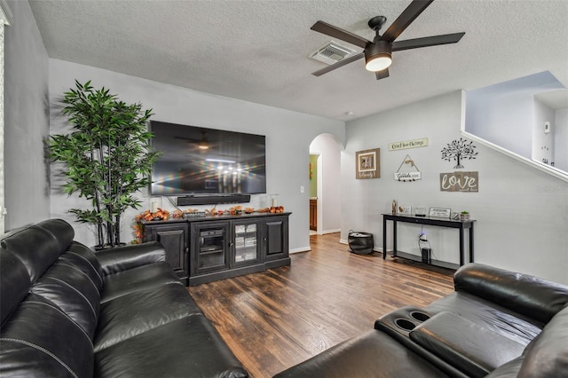 living room with a textured ceiling, visible vents, a ceiling fan, dark wood finished floors, and arched walkways