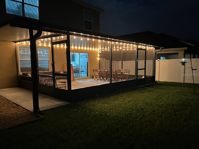 back of house at night featuring a yard, stucco siding, fence, and a patio area