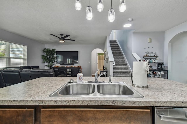 kitchen with pendant lighting, a textured ceiling, ceiling fan, a kitchen island with sink, and sink