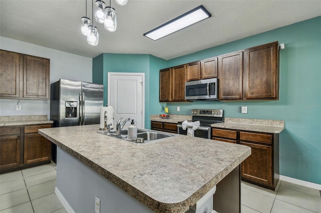 kitchen with an island with sink, sink, stainless steel appliances, and decorative light fixtures