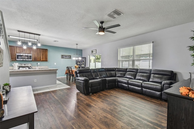 living room featuring ceiling fan with notable chandelier, visible vents, a textured ceiling, and dark wood-style floors
