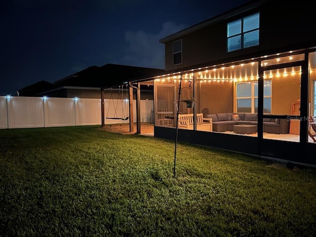 back of house at twilight with fence, stucco siding, outdoor lounge area, and a lawn