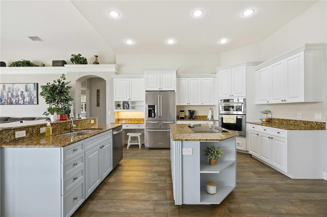 kitchen featuring white cabinets, an island with sink, stainless steel appliances, dark hardwood / wood-style floors, and dark stone counters