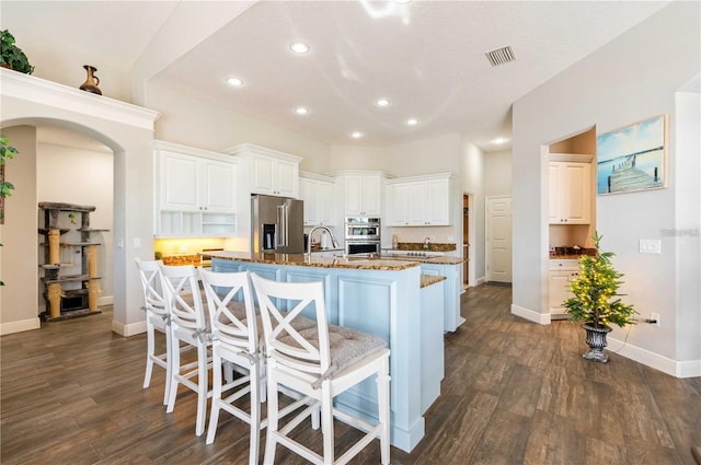 kitchen featuring appliances with stainless steel finishes, white cabinetry, a breakfast bar area, dark hardwood / wood-style flooring, and a center island with sink