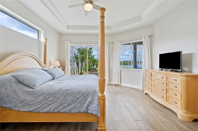 bedroom with light wood-type flooring, a tray ceiling, multiple windows, and access to exterior