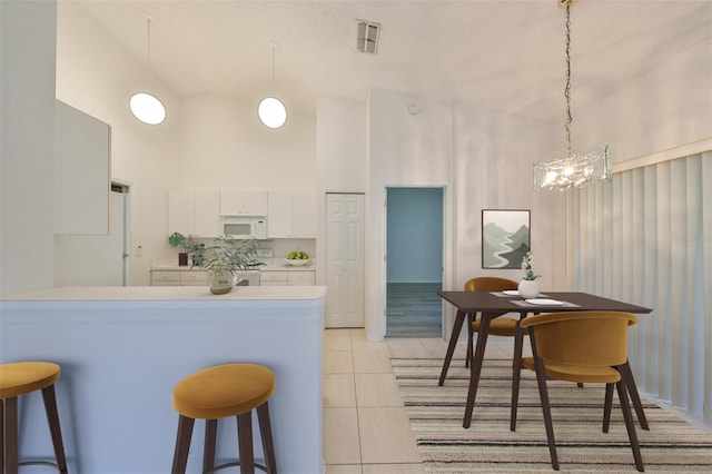 kitchen featuring white cabinets, decorative light fixtures, kitchen peninsula, and a high ceiling