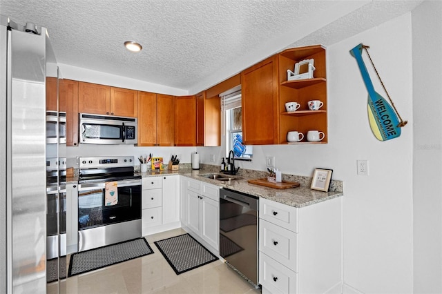 kitchen featuring appliances with stainless steel finishes, light stone counters, sink, white cabinetry, and light tile patterned flooring