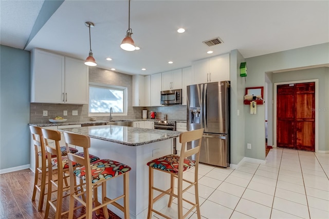 kitchen with appliances with stainless steel finishes, light stone countertops, a kitchen island, white cabinets, and pendant lighting