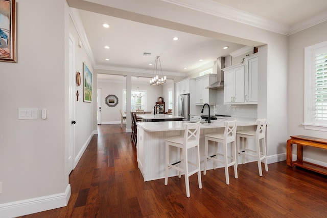 kitchen featuring wall chimney range hood, hanging light fixtures, white cabinetry, stainless steel refrigerator, and an inviting chandelier