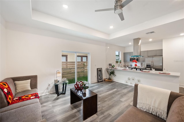 living room with ceiling fan, light hardwood / wood-style flooring, and a raised ceiling