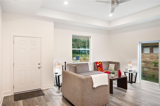 living room featuring light hardwood / wood-style flooring, a tray ceiling, and ceiling fan