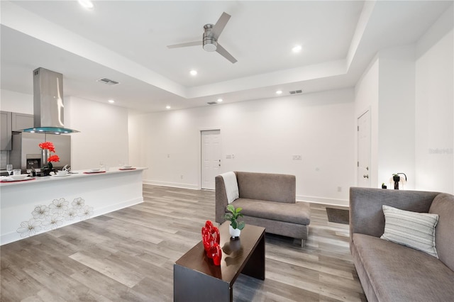 living room with ceiling fan, light wood-type flooring, and a raised ceiling