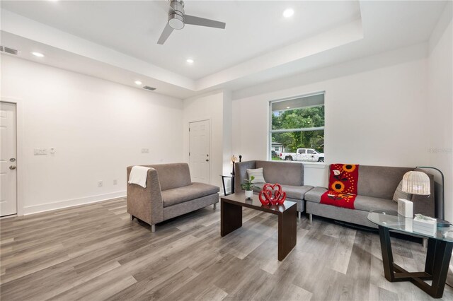 living room with ceiling fan, light hardwood / wood-style flooring, and a tray ceiling