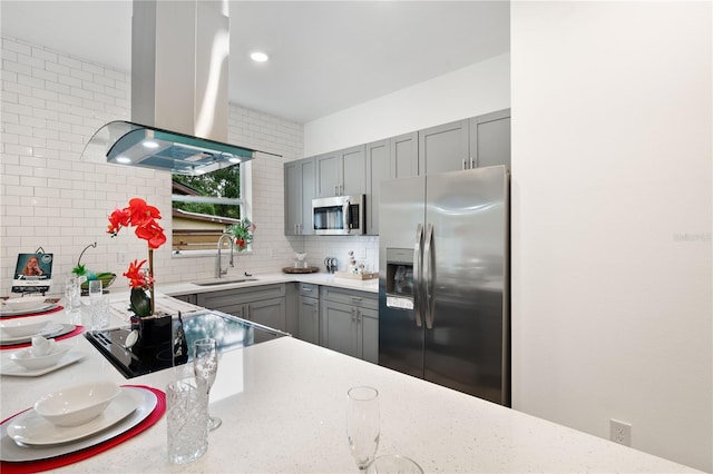 kitchen featuring gray cabinets, island range hood, stainless steel appliances, backsplash, and light stone countertops