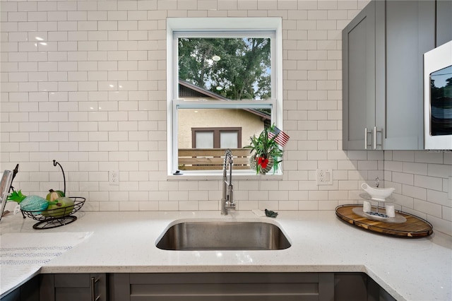 kitchen featuring gray cabinets, decorative backsplash, light stone countertops, and sink