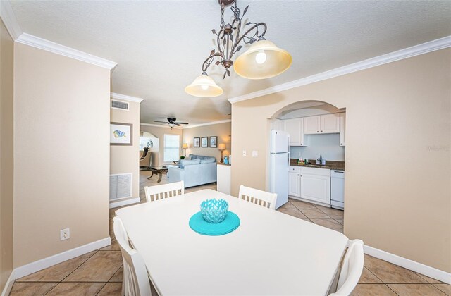 dining room featuring a textured ceiling, sink, light tile patterned floors, crown molding, and ceiling fan