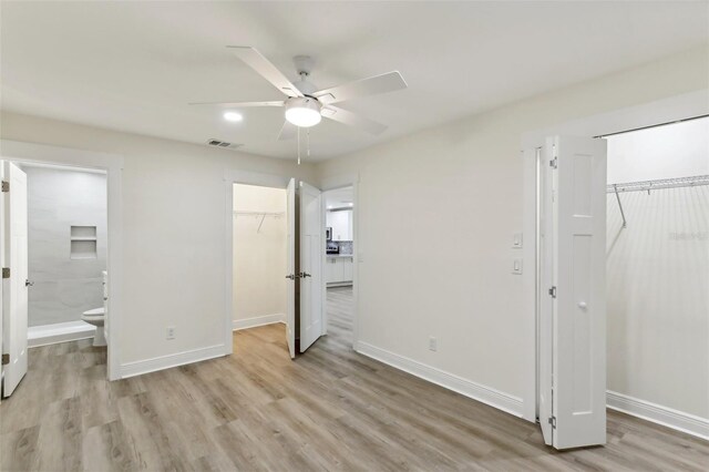 unfurnished bedroom featuring light hardwood / wood-style floors, a closet, connected bathroom, a spacious closet, and ceiling fan