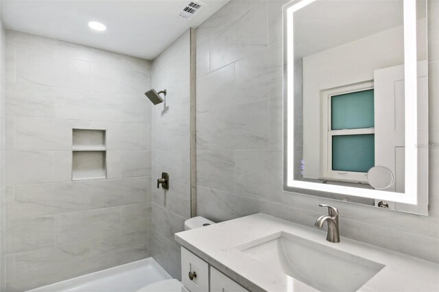 bathroom with toilet, vanity, and tiled shower