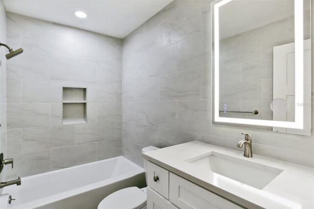 full bathroom with tiled shower / bath, vanity, tile walls, and toilet