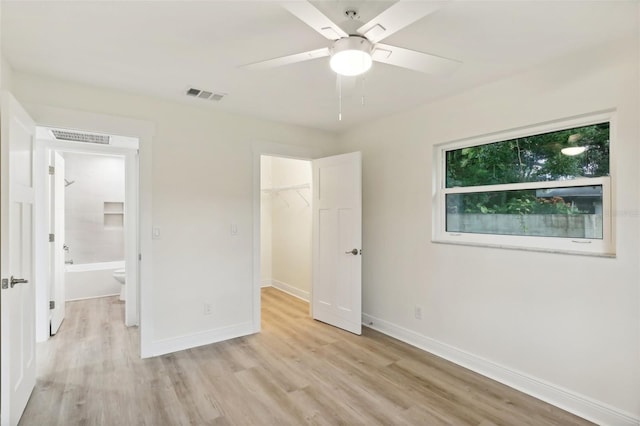 unfurnished bedroom featuring ceiling fan, light hardwood / wood-style floors, a closet, a spacious closet, and ensuite bathroom