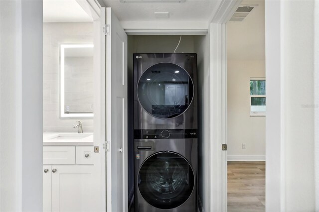 laundry room featuring light hardwood / wood-style floors, stacked washing maching and dryer, and sink