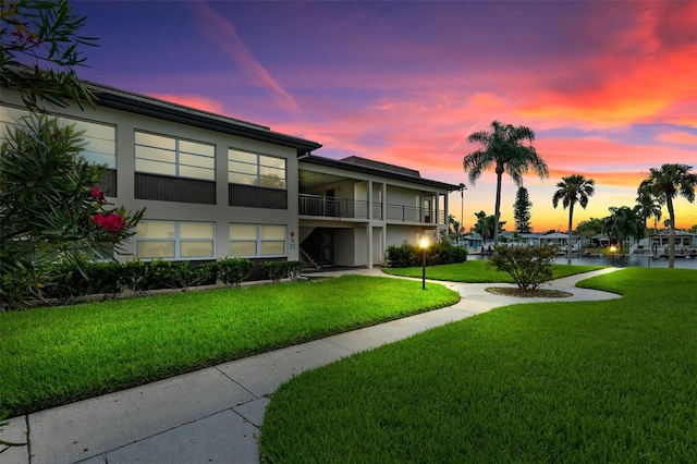 back house at dusk featuring a yard and a balcony