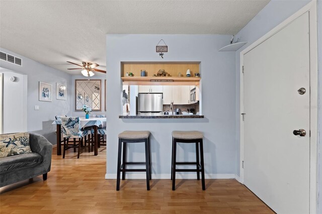 kitchen with ceiling fan, kitchen peninsula, light hardwood / wood-style flooring, stainless steel appliances, and a kitchen breakfast bar