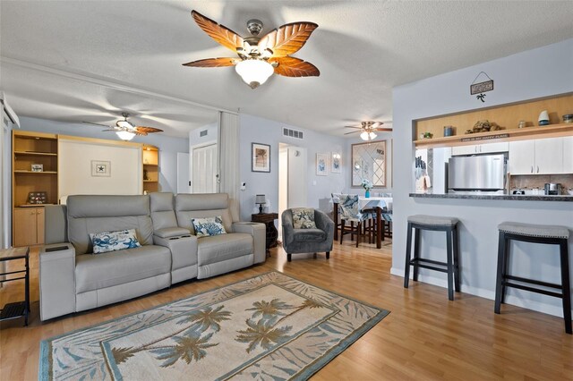 living room featuring ceiling fan, a textured ceiling, and light hardwood / wood-style flooring