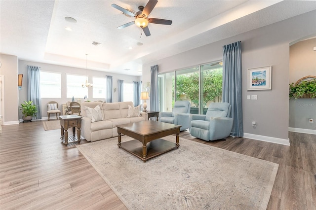 living room featuring a healthy amount of sunlight, a tray ceiling, hardwood / wood-style floors, and ceiling fan