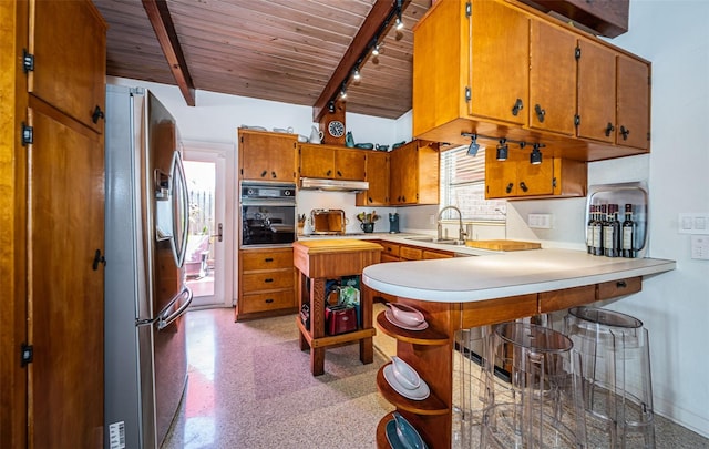 kitchen with wood ceiling, beam ceiling, kitchen peninsula, black oven, and stainless steel refrigerator with ice dispenser