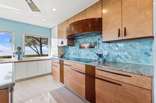 kitchen featuring tasteful backsplash, light stone countertops, custom range hood, modern cabinets, and black electric cooktop