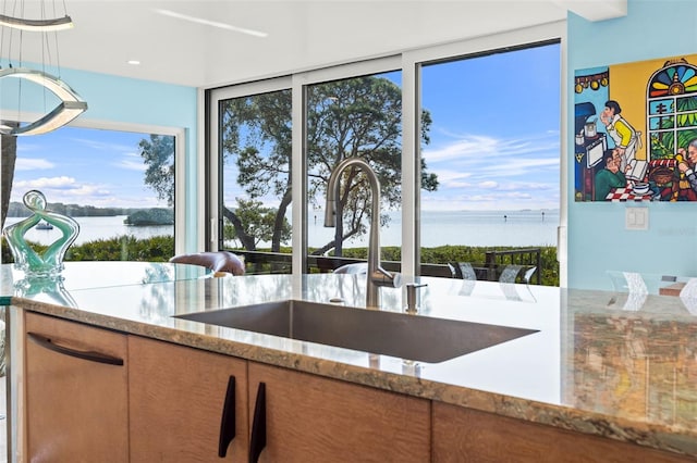 kitchen with a water view, a sink, and light stone countertops