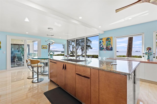 kitchen with a kitchen island with sink, sink, pendant lighting, and light stone counters