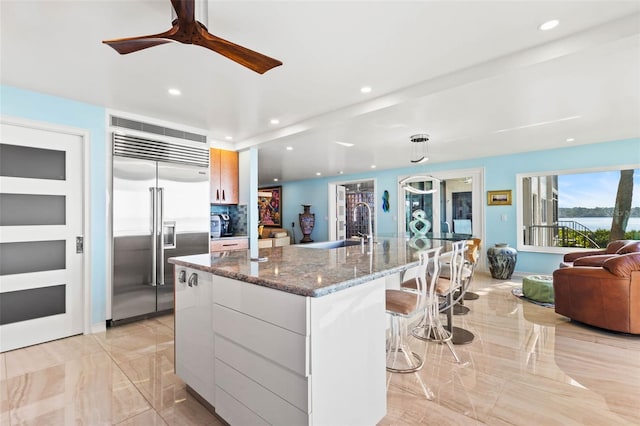 kitchen with a spacious island, modern cabinets, dark stone countertops, stainless steel built in fridge, and white cabinetry