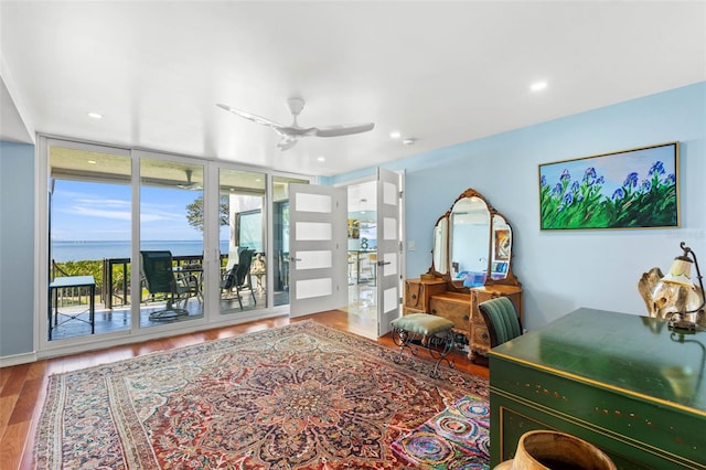 interior space featuring floor to ceiling windows, ceiling fan, a water view, and wood-type flooring