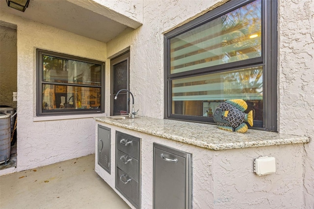 kitchen featuring a textured wall, concrete flooring, a sink, and light stone countertops