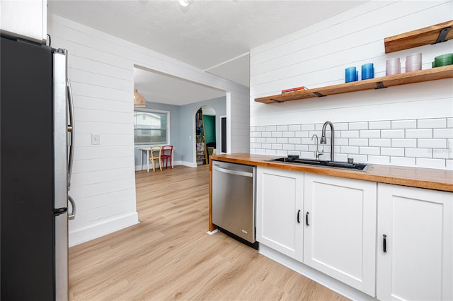 kitchen with light wood-type flooring, sink, white cabinetry, stainless steel appliances, and butcher block countertops