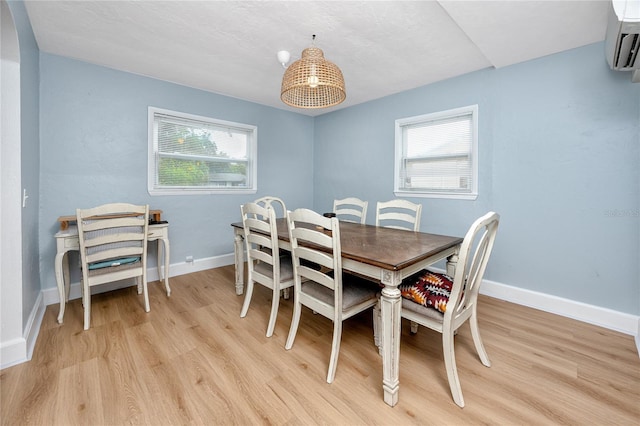 dining room featuring a wall unit AC, a healthy amount of sunlight, and light wood-type flooring