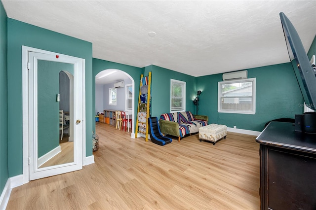 living room featuring a wall mounted AC, a textured ceiling, and light wood-type flooring