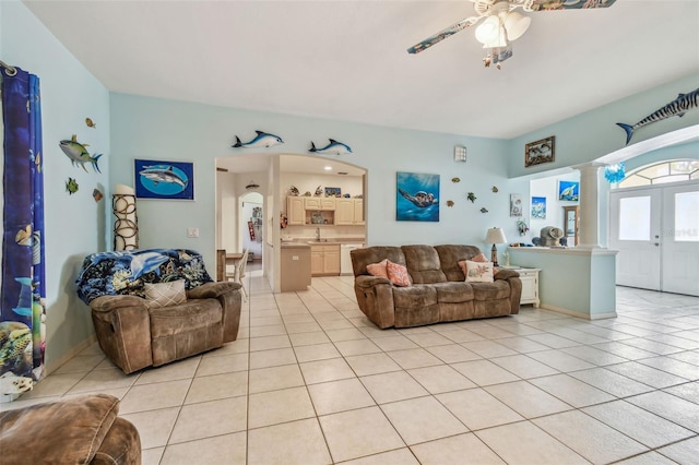 living area featuring light tile patterned flooring, decorative columns, arched walkways, and ceiling fan