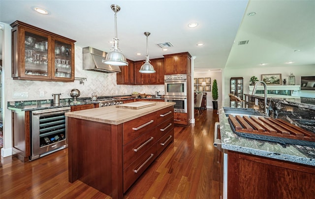 kitchen with appliances with stainless steel finishes, dark hardwood / wood-style flooring, wine cooler, a kitchen island, and exhaust hood