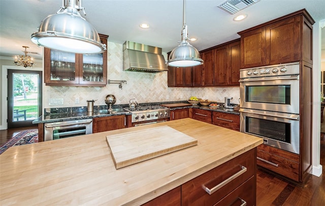 kitchen featuring butcher block counters, decorative light fixtures, dark hardwood / wood-style flooring, appliances with stainless steel finishes, and wall chimney range hood