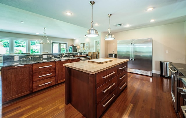 kitchen featuring pendant lighting, stainless steel refrigerator, a center island, sink, and dark hardwood / wood-style floors