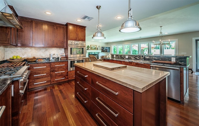 kitchen with wooden counters, a center island, dark hardwood / wood-style floors, wall chimney exhaust hood, and appliances with stainless steel finishes