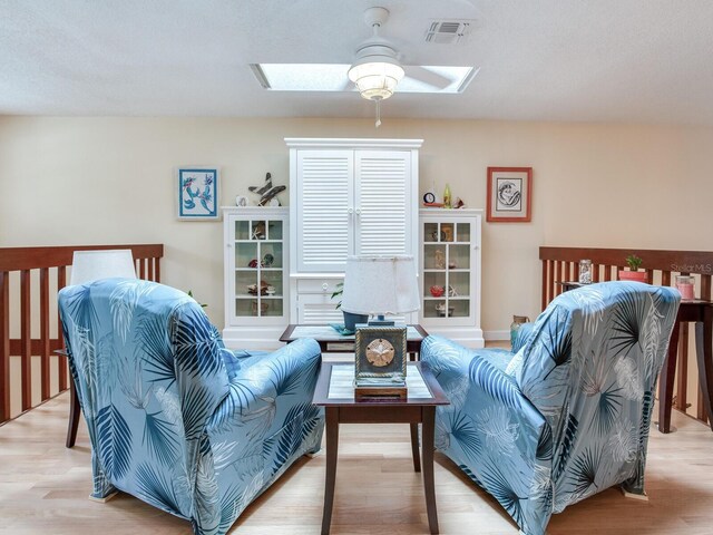 living room with a textured ceiling, ceiling fan, light wood-type flooring, and a skylight