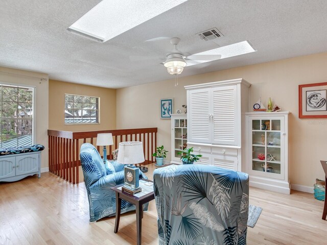 living room featuring a skylight, ceiling fan, light hardwood / wood-style floors, and a textured ceiling