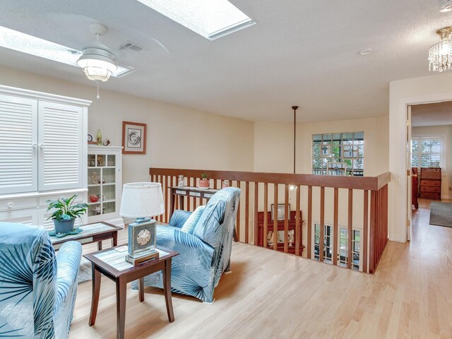 living area with a textured ceiling, ceiling fan, light wood-type flooring, and a skylight