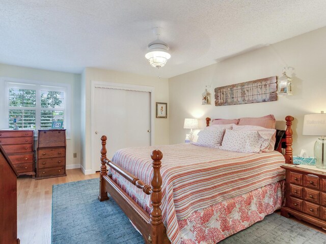 bedroom with a textured ceiling, ceiling fan, a closet, and light hardwood / wood-style floors