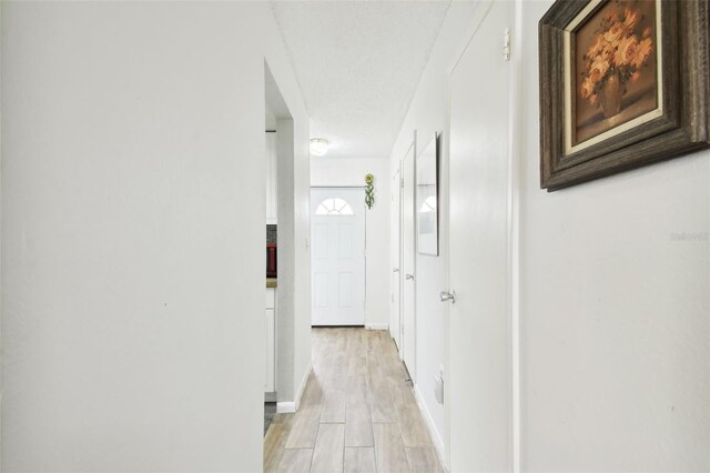 corridor with a textured ceiling and light hardwood / wood-style floors